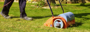 Belästigung mit einem Panikmacher. Rasen Sie den Täter in Aktion. Mit einem Panzer im Garten zur Verbesserung der Qualität des Rasen im Frühling. ein Arbeiter, Gardener Operationsbodenverbrennungsmaschine auf Grasrasen.